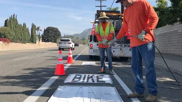 Workers painting "Bike Lane" on a road
