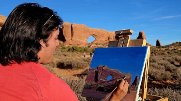 a person is painting on an easel in the desert