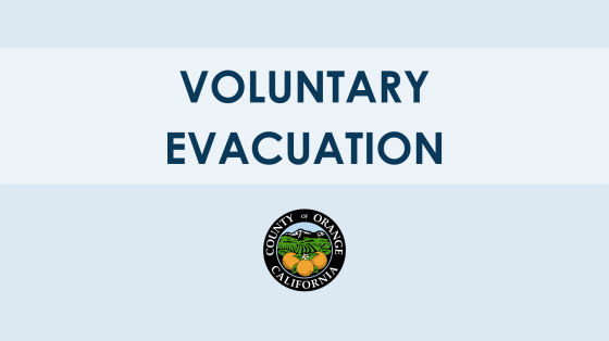 The image contains a message that reads "VOLUNTARY EVACUATION" in bold, dark blue capital letters against a light blue gradient background. Below the text, there is the official seal of Orange County, California.