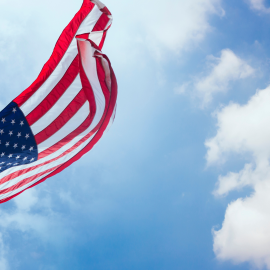 an american flag waving in the wind against a blue sky