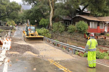 Orange County Public Works employee watches excavator clear a road blocked by debris flow.