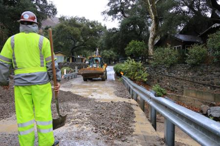 OC Public Works worker stands amid debris flow with a loader in the background.